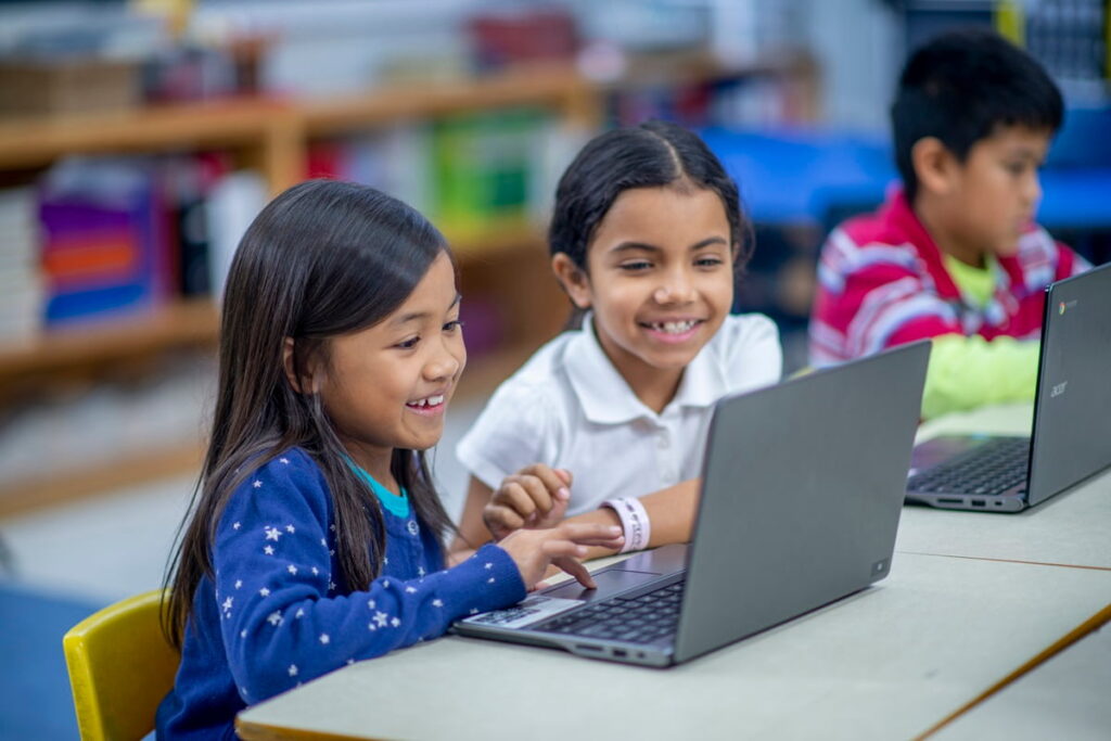 Two elementary students work together on laptops during computer lab