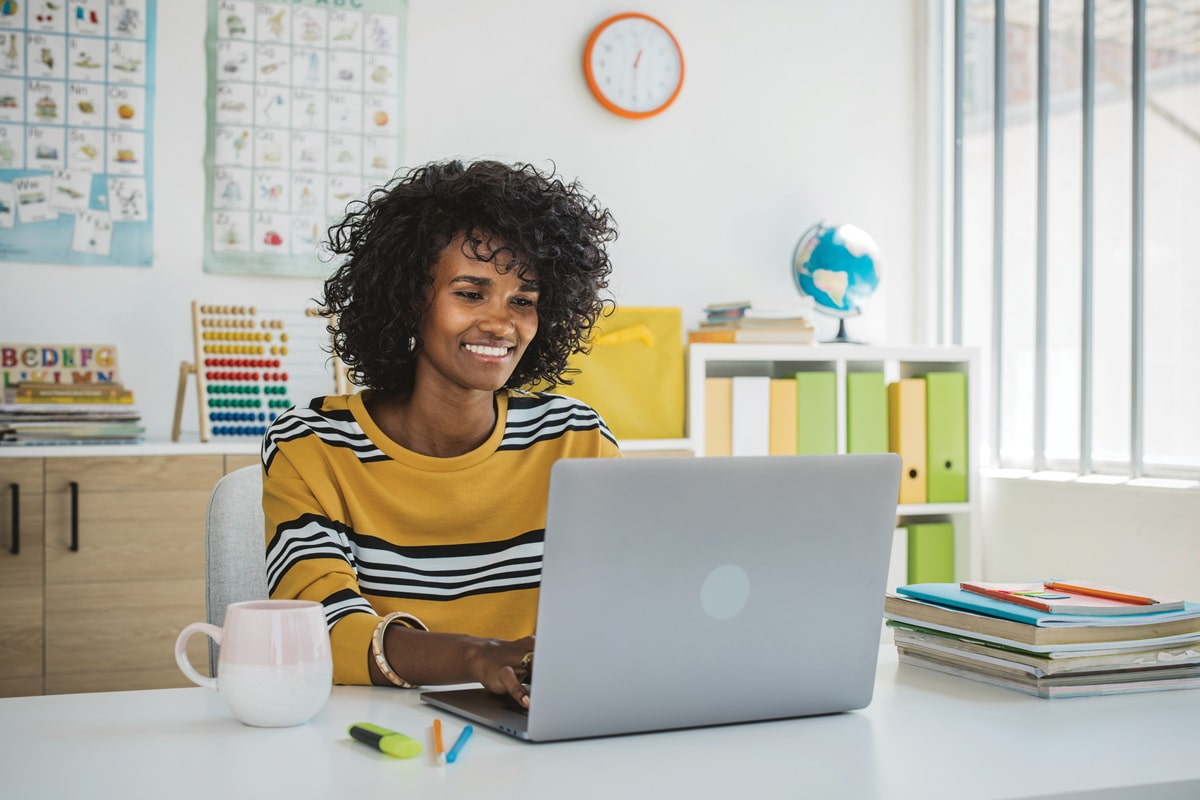 Teacher in classroom at desk on laptop for students video call