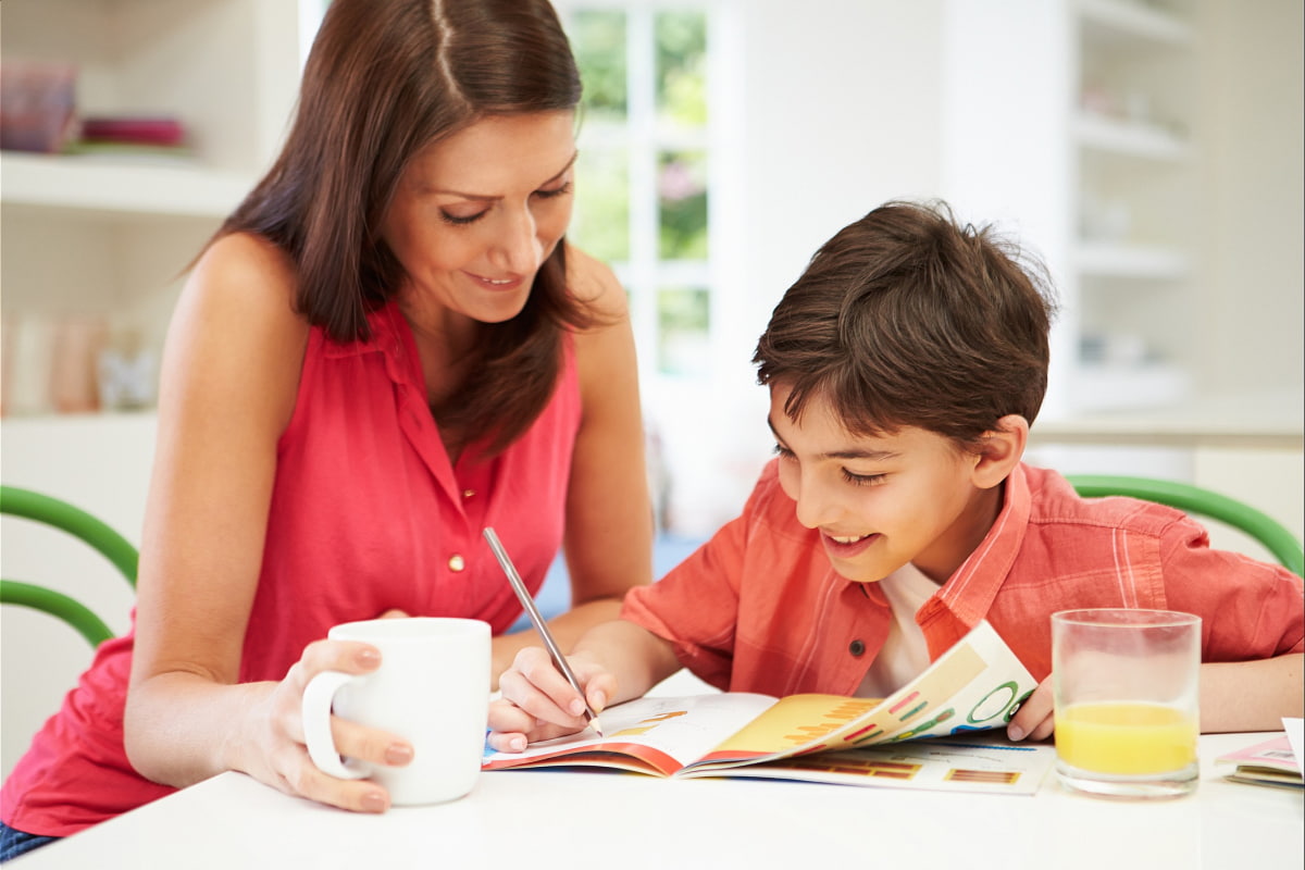 mother helping son write in journal during school break