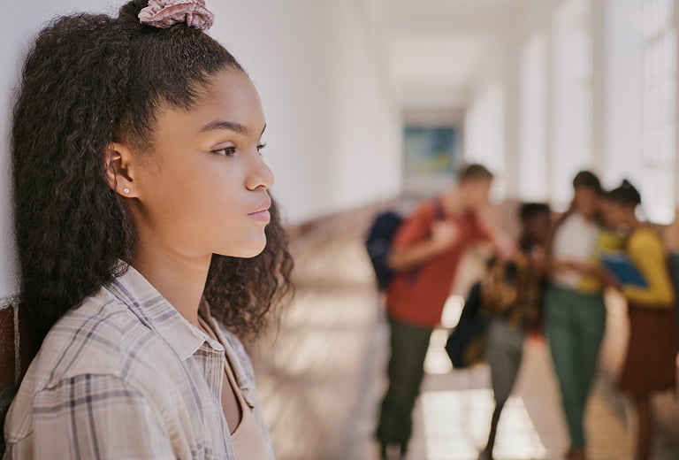 Sad teenage girl at school back against wall feeling excluded